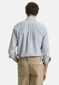 Gestreiftes Langarmhemd in Hellblau und Weiß, aus Baumwolle, mit einem Button-Down-Kragen und aufgerollten Manschetten. Kombiniert mit beigen Hosen.