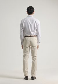 Chinos de color claro y una camisa a rayas, con corte recto. Cinturón de cuero marrón y zapatos oscuros. Fondo neutro.