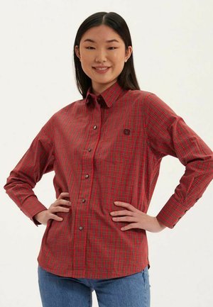 Chemise à carreaux rouge et noire à manches longues, avec col, boutons contrastants et un petit logo sur la poitrine.