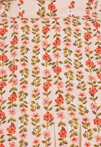 Tissu rose clair avec des motifs verticaux de petites fleurs rouges et roses ainsi que des feuilles vertes, disposés en rangées et plis.