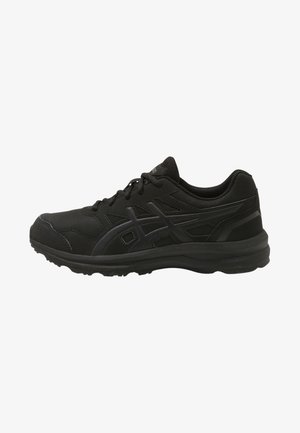 Chaussure de sport basse noire à lacets sur le devant, semelle texturée et surcouches à motifs discrets sur les côtés.
