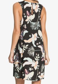 Robe noire sans manches avec un motif floral tropical aux couleurs pastel, portée par une femme vue de dos.
