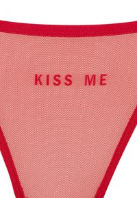 String en résille rouge avec une ceinture élastique. Présente le texte "KISS ME" en lettres majuscules, centré à l'arrière. La couleur du texte correspond à celle du tissu.