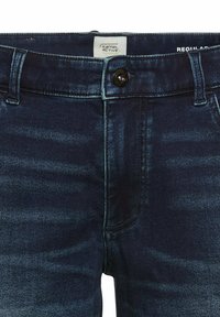 Jeans en denim indigo foncé avec une coupe régulière, présentant une fermeture à bouton, des poches avant et de légers dégradés sur le tissu.