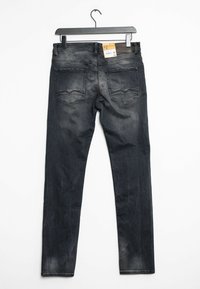 Jeans de mezclilla oscuros ajustados con un ligero desgaste, diseño de cinco bolsillos y un parche de cuero en la cinturilla. Cuélga en una percha de metal negro.