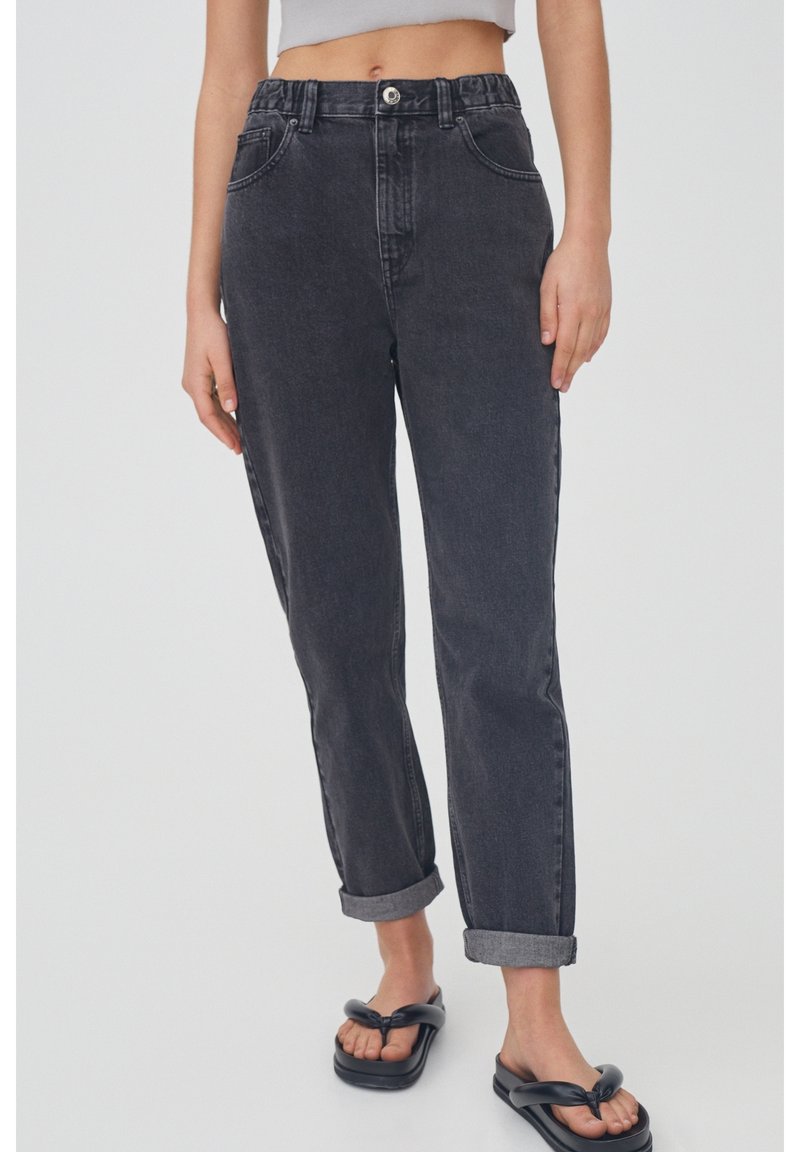 Jeans noirs taille haute avec revers, fabriqués en denim. Comprennent des poches avant et une fermeture à bouton métallique. Texture lisse.