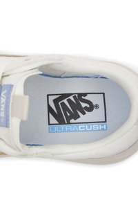Innenansicht eines weißen Sneakers mit dem "VANS"-Logo in Schwarz und "ULTRA CUSH" in Blau. Glatte Stoffstruktur und gepolsterter Kragen für Komfort.