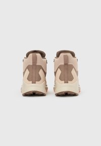 Ζευγάρι μπεζ και καφέ ορειβατικά μποτάκια, εμφανιζόμενα από πίσω σε απλό λευκό φόντο.