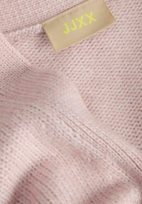 Jersey de punto rosa claro con un patrón texturizado. La etiqueta muestra "JJXX" en amarillo sobre una etiqueta de tela beige.