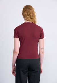 Bordo uska majica kratkih rukava s okruglim izrezom, uparena s crnim hlačama. Glatka tekstura, minimalistički dizajn, bez vidljivih uzoraka.
