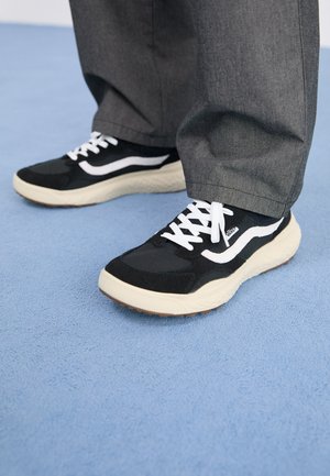 Black and white sneaker featuring a textured upper, round toe, white laces, and a thick cream-colored sole with a patterned bottom.
