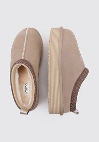 Zapatos slip-on beige con parte superior de ante, forrados con piel de oveja, que presentan una banda texturizada cosida y una suela de goma con diseño de estrías.