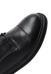 Chaussure en cuir noir avec un bout rond, design à lacets, accents cousus et texture lisse. Semelle en caoutchouc épaisse pour plus de durabilité.