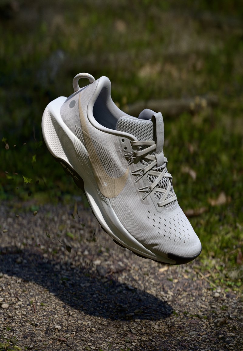 Baskets de sport beige clair avec une tige en maille texturée, des lacets plats et un logo swoosh visible. Présentent une semelle rembourrée pour un bon soutien.