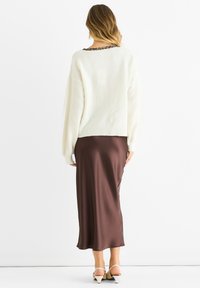 Maglione bianco lavorato a maglia con un collo stampa leopardata, abbinato a una gonna midi in raso marrone liscia. L'accostamento è completato da sandali beige con tacco.