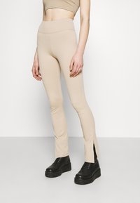 Beiga ribbade byxor med sidoklyftor vid fållen, kombinerade med kraftiga svarta snörboots. Mjuk tyg, figurnära design.