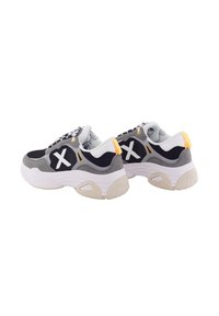 Zapatillas con una parte superior de malla gris y negra, acentos blancos y un tirador en el talón de color amarillo. Suela blanca gruesa con detalles texturizados en beige.