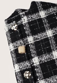 Tissu tweed à carreaux noir et blanc avec trois boutons décoratifs : un doré texturé, un tissé noir et blanc, un géométrique doré et blanc.