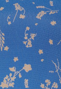 Blått tyg med en texturerad yta, som pryds av beige blommönster och stjärnmönster, vilket ger en dekorativ design.