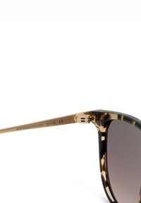 Zonnebril met een montuur van schildpadmotief en gouden metalen poten, met scharnier en maatmarkeringen op het pootje.