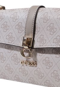 Borsa a tracolla beige con motivo, dotata di logo metallico, tracolla in pelle liscia e dettagli in hardware dorato. Tessuto testurizzato con forma strutturata.