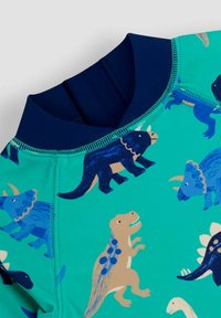 Rash guard pour enfants en tissu turquoise avec des motifs de dinosaures colorés. Il possède un col marine et une texture lisse.