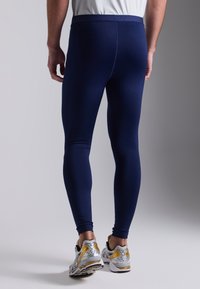 Marineblauwe sportlegging met een gladde textuur en een elastische tailleband, gecombineerd met zilveren en gouden hardloopschoenen.