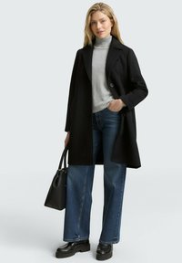 Cappotto di lana nero con un solo bottone, maglione a collo alto grigio, jeans blu a gamba larga e scarpe platform nere, abbinato a una borsa nera.