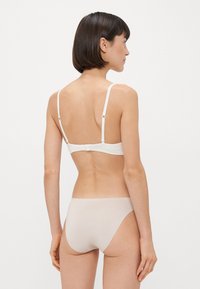 Biały stanik braletka z cienkimi ramiączkami i zapięciem na haftkę; zestawiony z jasnobeżowymi, bezszwowymi majtkami. Gładki materiał, prosta forma, minimalne akcenty.
