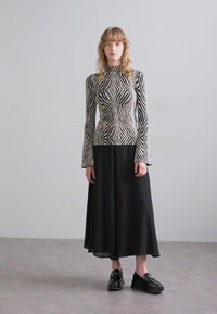 Maglione a maniche lunghe con un motivo zigzag bianco e nero; abbinato a una gonna midi plissettata nera e scarpe con piattaforma nere.