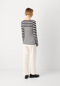 Svartvit randig långärmad topp, kombinerad med vita vida byxor och svarta skor. Slät tyg och åtsittande design med rund halsringning.