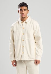 Crème kleurige jack van katoen, met een spreidcol en twee voorzakken, en houten knopen. Lange mouwen met een relaxte pasvorm.