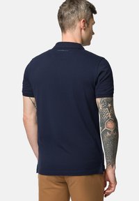 Granatowa koszulka polo z lekkiego materiału, z krótkimi rękawami, klasycznym kołnierzykiem i subtelnym logo z tyłu. Gładka faktura.
