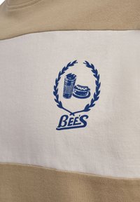 Beige og hvid stribet sweatshirt med et blåt grafik af en drink, hotdog og laurbærkrans, mærket "BEES." Blød bomulds tekstur.