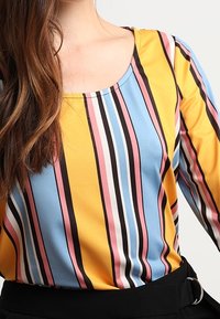 Flerfärgad långärmad topp med vertikala ränder i gult, blått, rosa och svart. Mjuk tyg med rund halsringning och avslappnad passform.
