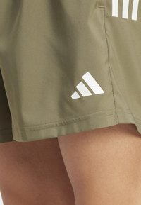 Olive green shorts with a smooth texture, featuring white three-stripe branding on the hemline and side seam.