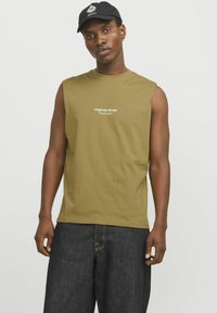Ærmeløs olivengrøn T-shirt med rund halsudskæring og hvid tekst "Originals Studio". Båret med mørk denimshorts og en sort kasket.