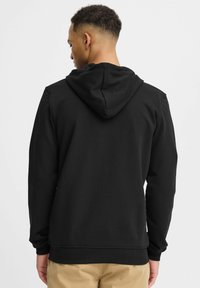 Sweatshirt à capuche noir en tissu texturé, coupe décontractée, avec des poignets et un ourlet en bords côtes. Doté d'une poche kangourou et sans graphismes visibles.