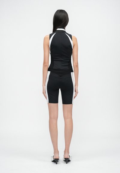 Černý sportovní outfit se bezramenným topem a šortkami, který má bílé boční detaily a přiléhavý střih. Hladká textura látky.