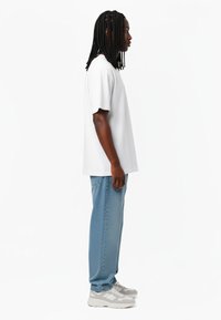 Bjela majica kratkih rukava u kombinaciji s svijetloplavim običnim trapericama i sivim sportskim cipelama, s opuštenim krojem i jednostavnim dizajnom.