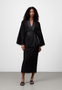 Zwart, met vachttextuur kimono-jack met satijnen afwerking, gecombineerd met een bijpassende kokerrok. Inclusief een strikceintuur en platte zwarte sandalen.