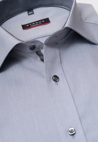 Helles graues Hemd mit Knopfleiste aus glattem Stoff, mit modernem Schnitt, schwarzen Knöpfen und einem kontrastierenden Kragenfutter im gestreiften Muster.