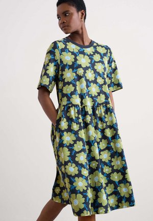 Kurzes Kleid aus dunklem Stoff, verziert mit großen grünen und blauen Blumenmustern, mit einem gerafften Taillenbereich und seitlichen Taschen.
