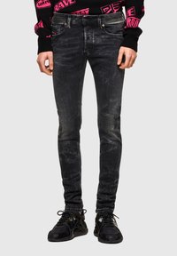 Jeans ajustados negros con acabado desteñido, con un sutil efecto desgastado, diseño de cinco bolsillos y cierre de cremallera. Combinados con zapatillas negras.