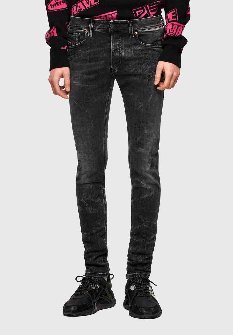 Jeans ajustados negros con acabado desteñido, con un sutil efecto desgastado, diseño de cinco bolsillos y cierre de cremallera. Combinados con zapatillas negras.