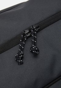 Black fabric zipper with double pull tabs and textured surface. Black cords with white accents are tied in knots at each pull tab.