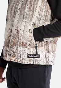 Weste mit Birchbaum-Print, durchgehend mit Reißverschluss, schwarzen Ärmeln und Timberland-Logopatch am Saum. Textiles Material mit Isolierung.