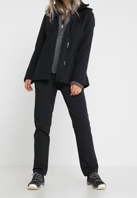 Black waterproof jacket with a hood over a gray zip-up midlayer, paired with black pants and gray athletic shoes. Simple design, functional details.