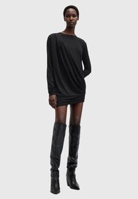 Abito nero a maniche lunghe con design drappeggiato e dettagli arricciati, abbinato a stivali neri in pelle al ginocchio con tacco a blocco.