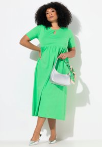 Vihreä keskipitkä mekko avainaukolla, lyhyillä hihoilla ja liehuvalla hameella. Yhdistettyinä hopeiseen käsilaukkuun ja metallisiin korkokenkiin.